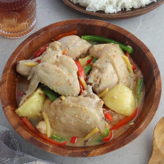 Ginataang Manok with potatoes and bell peppers in a wooden bowl with a plate of rice on the side