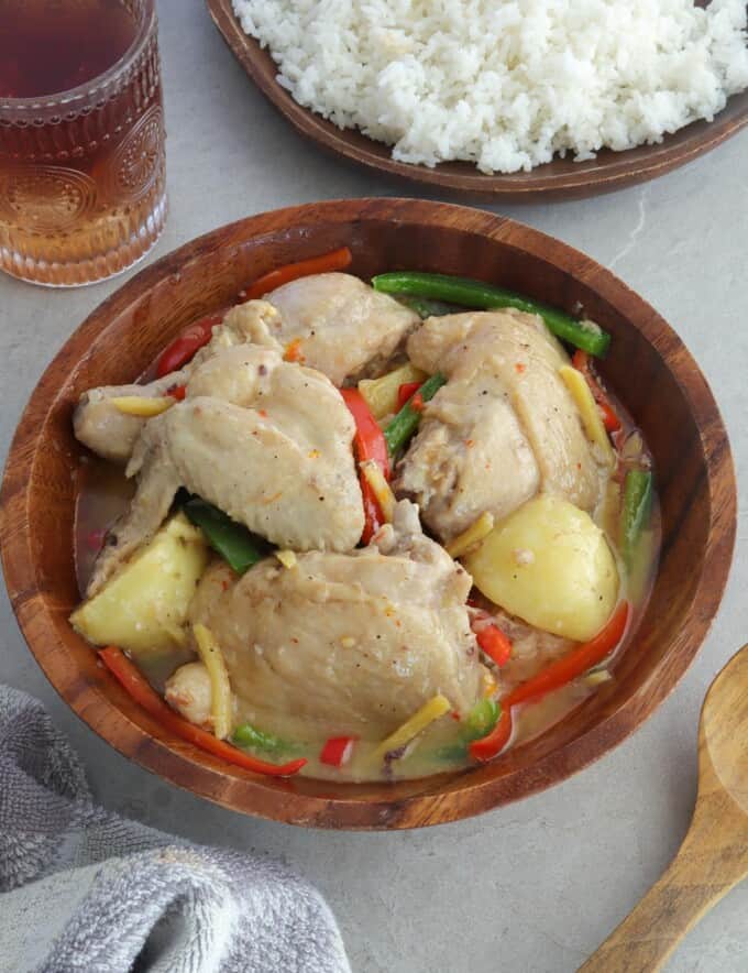 Ginataang Manok with potatoes and bell peppers in a wooden bowl with a plate of rice on the side