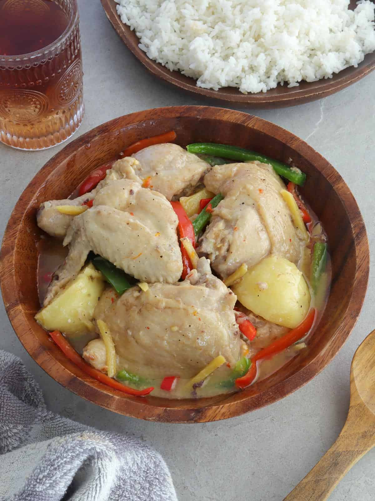 Ginataang Manok with potatoes and bell peppers in a wooden bowl with a plate of rice on the side