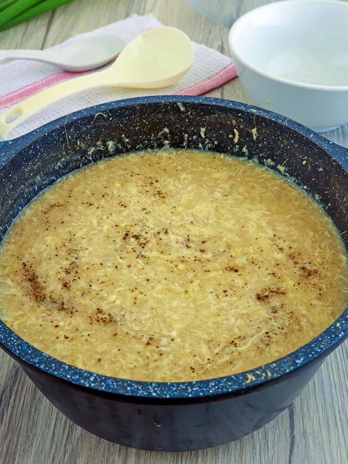 Chicken Corn Soup in a blue pot with spatulas in the background.