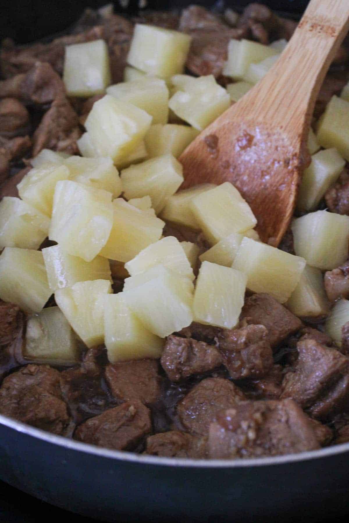 stirring pineapple chunks with pork in a skillet