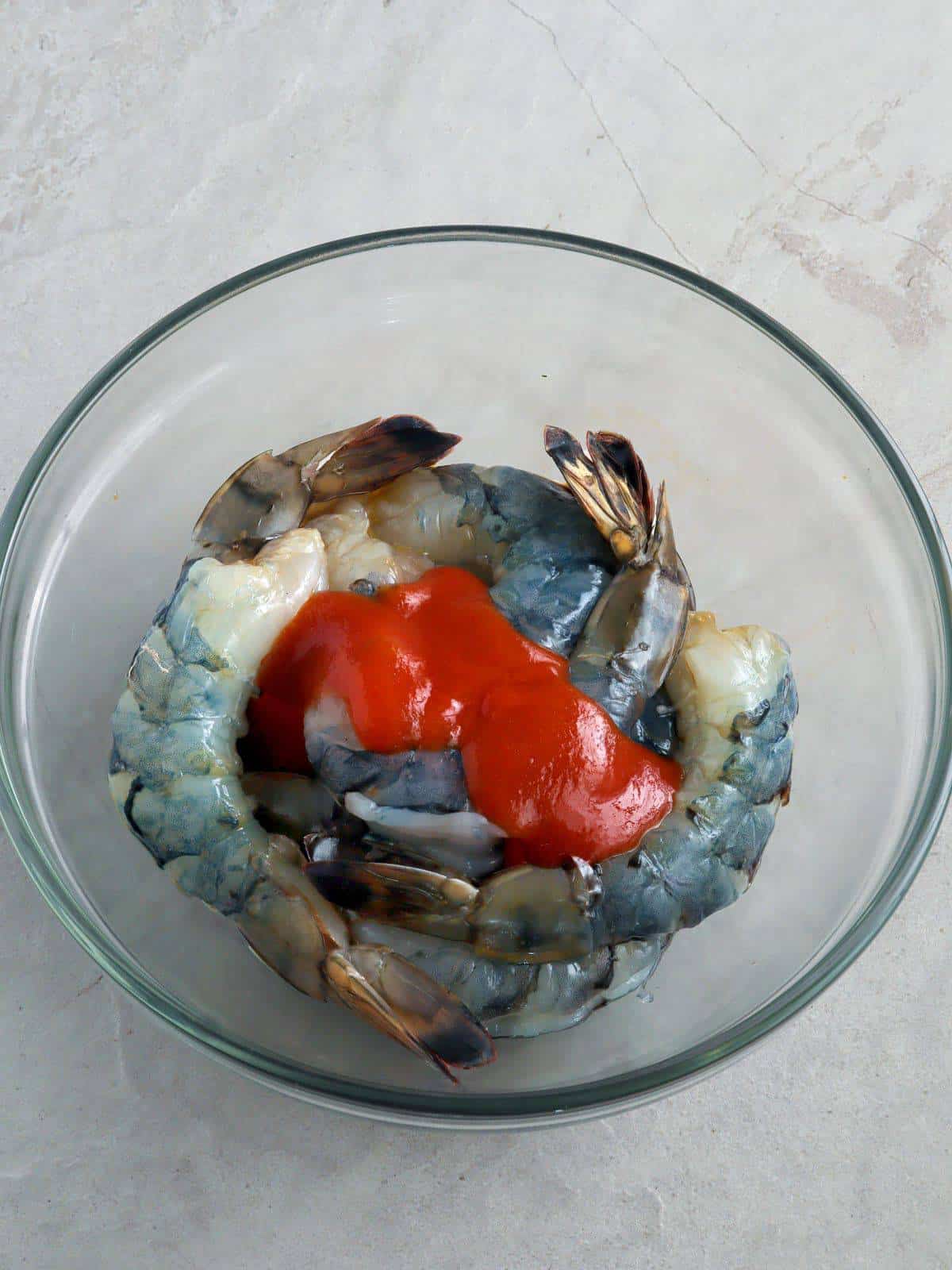 peeled shrimp marinating in Sriracha sauce in a glass bowl