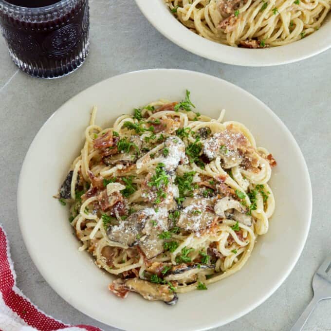 Filipino-style Pasta Carbonara on white plates with a glass of juice in the background.