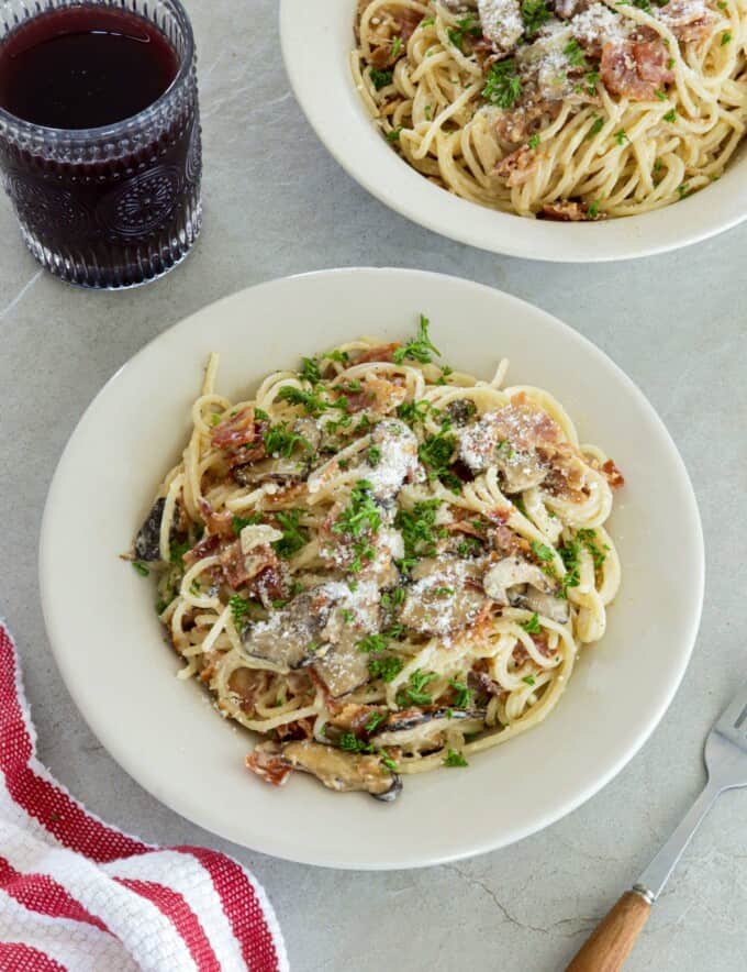 Filipino-style Pasta Carbonara on white plates with a glass of juice in the background.