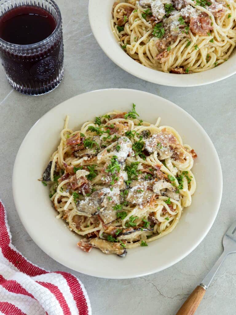 Filipino-style Pasta Carbonara on white plates with a glass of juice in the background.