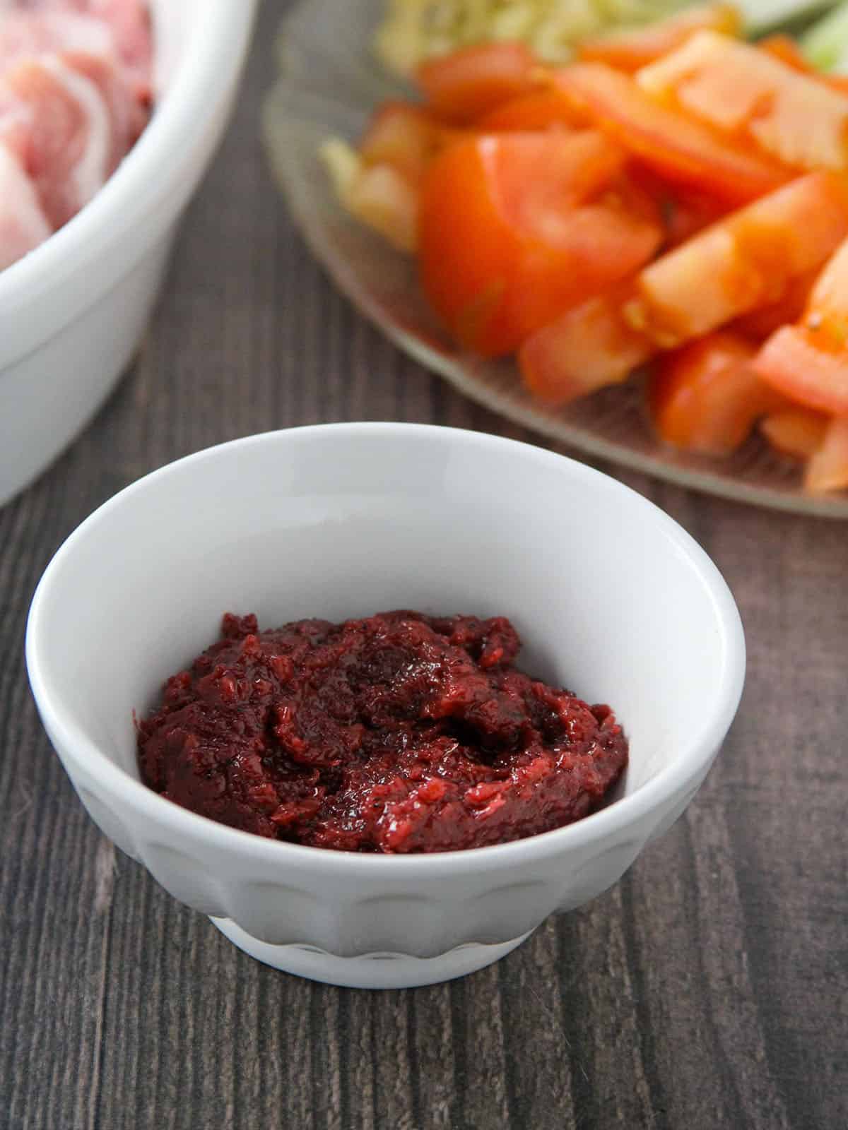 sauteed shrimp paste in a white bowl with chopped tomatoes on the side