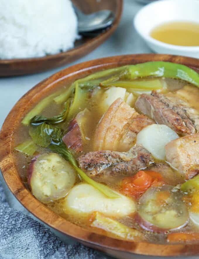 sinigang with grilled pork belly in a serving bowl with a side of steamed rice and fish sauce
