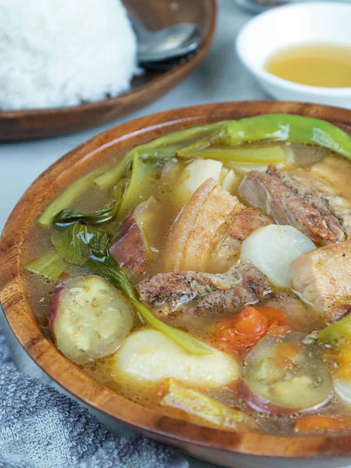 sinigang with grilled pork belly in a serving bowl with a side of steamed rice and fish sauce