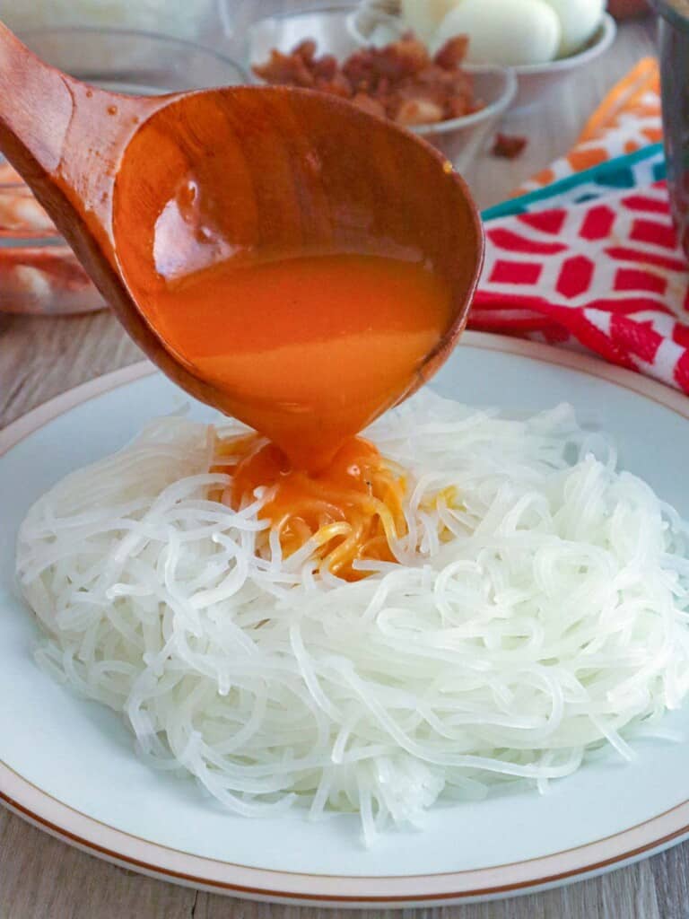 pouring shrimp sauce over a plate of rice noodles
