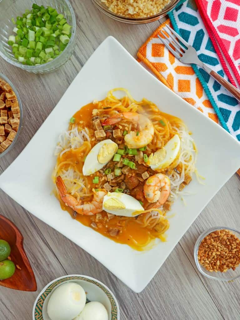 pancit palabok with eggs, shrimp, and sauce on a plate