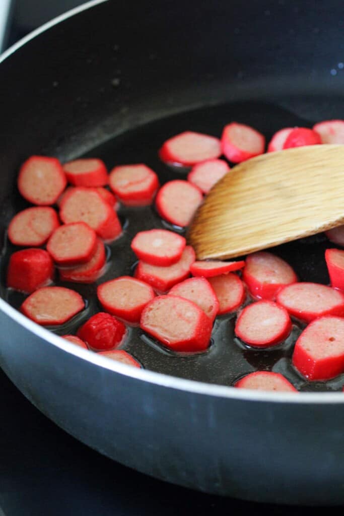 browning sliced Filipino red hot dogs in a skillet