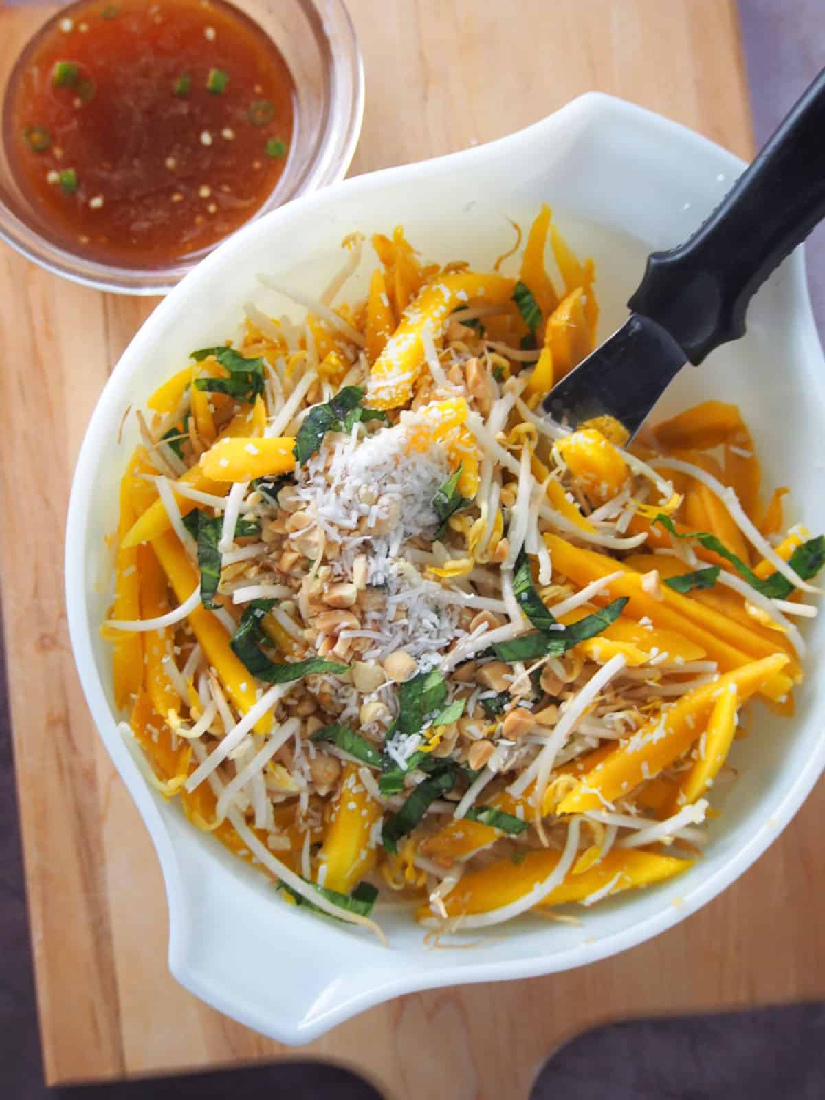 mixing Thai mango salad in a white bowl