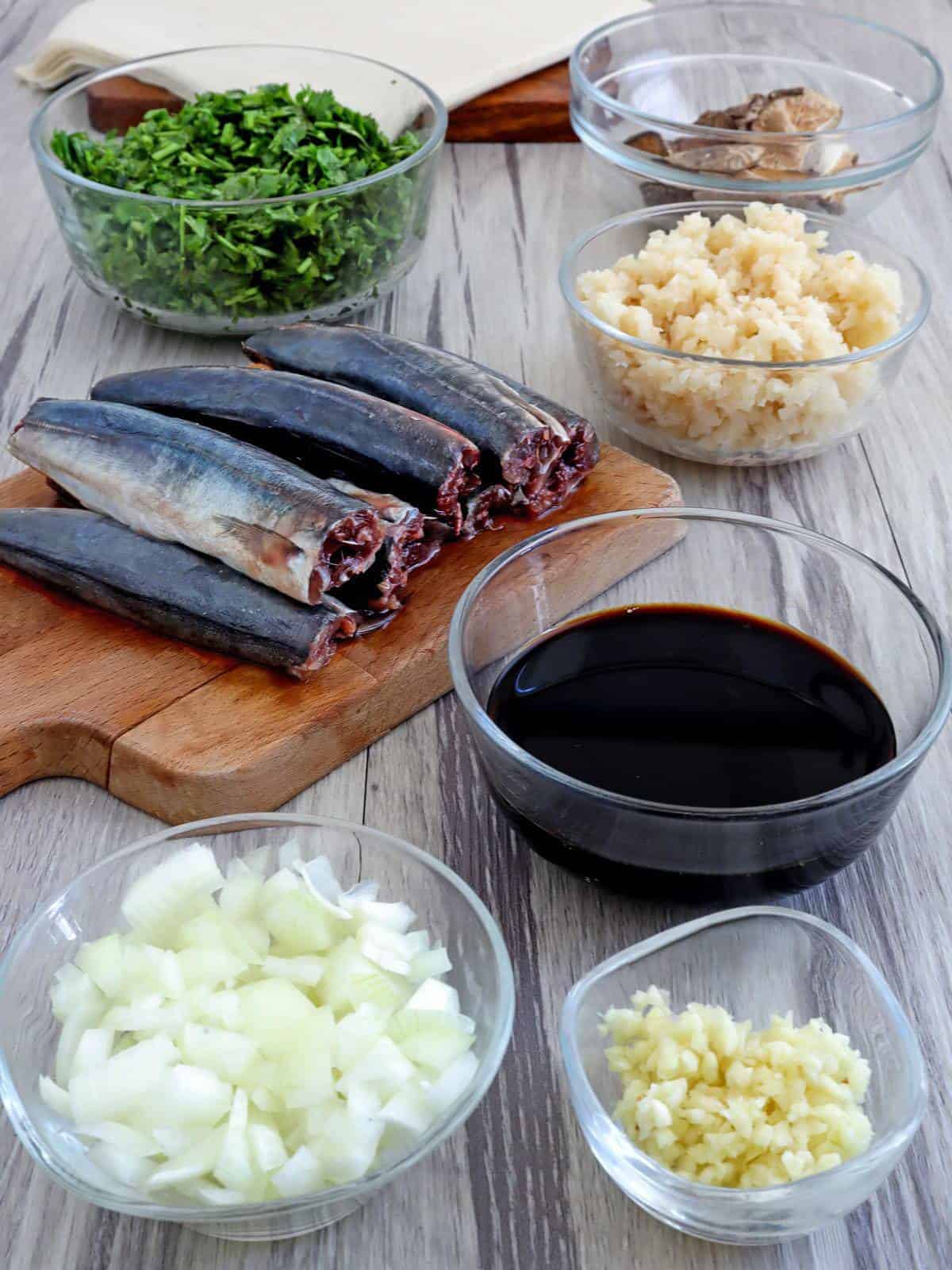 cleaned round scad fish on a cutting board and soy sauce, chestnuts, onions, Chinese celery, garlic in individual bowls