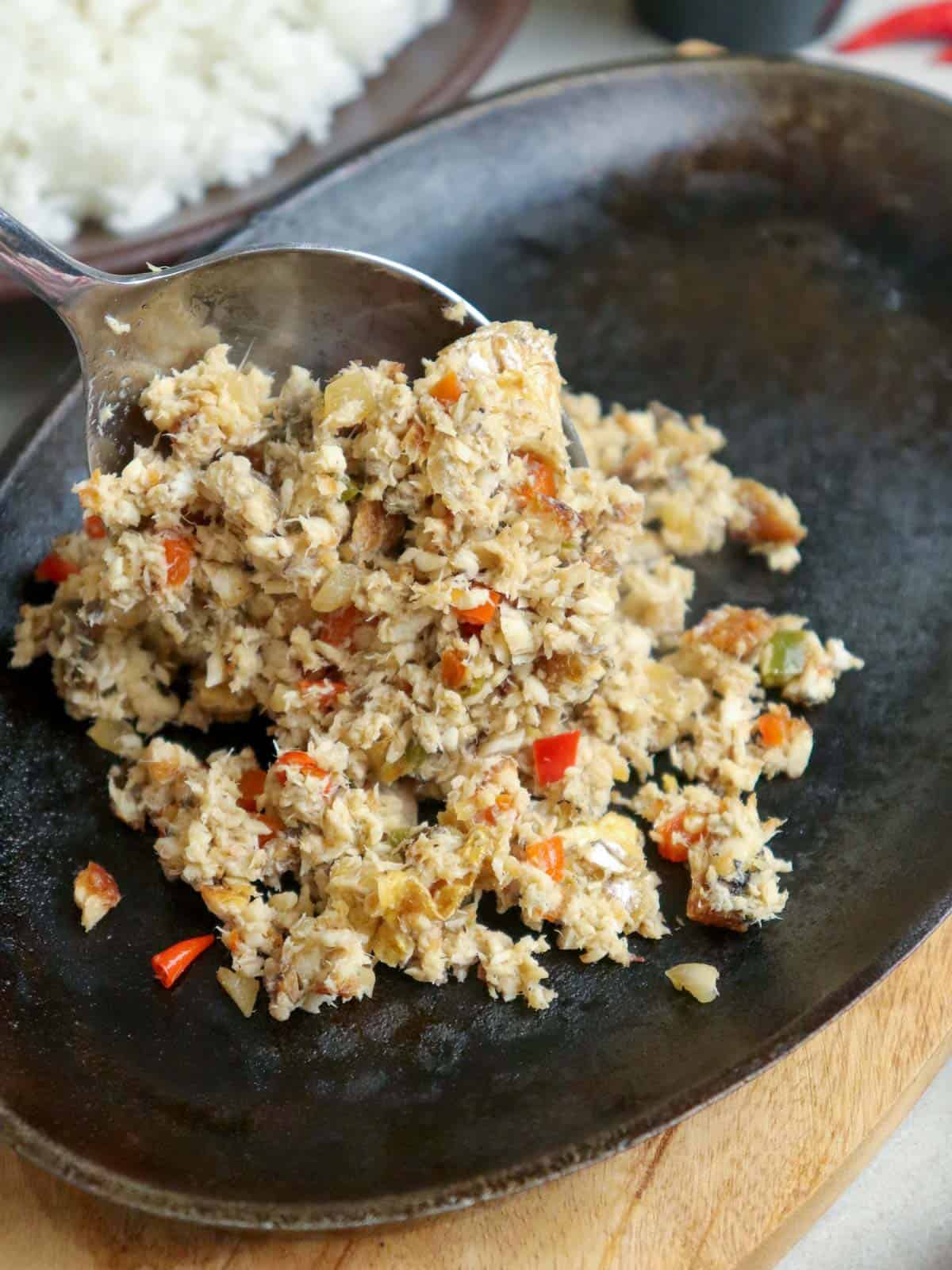 serving fish sisig with a spoon on a cast iron skillet