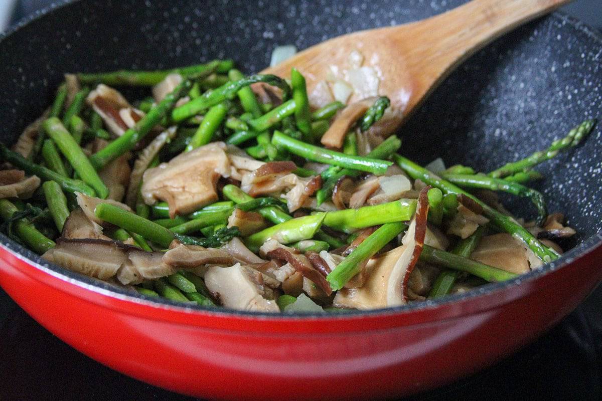 stir-frying mushrooms and asparagus in a red wok