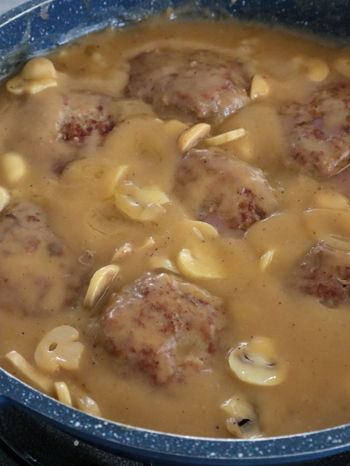 burger steak in a pan with mushroom sauce.