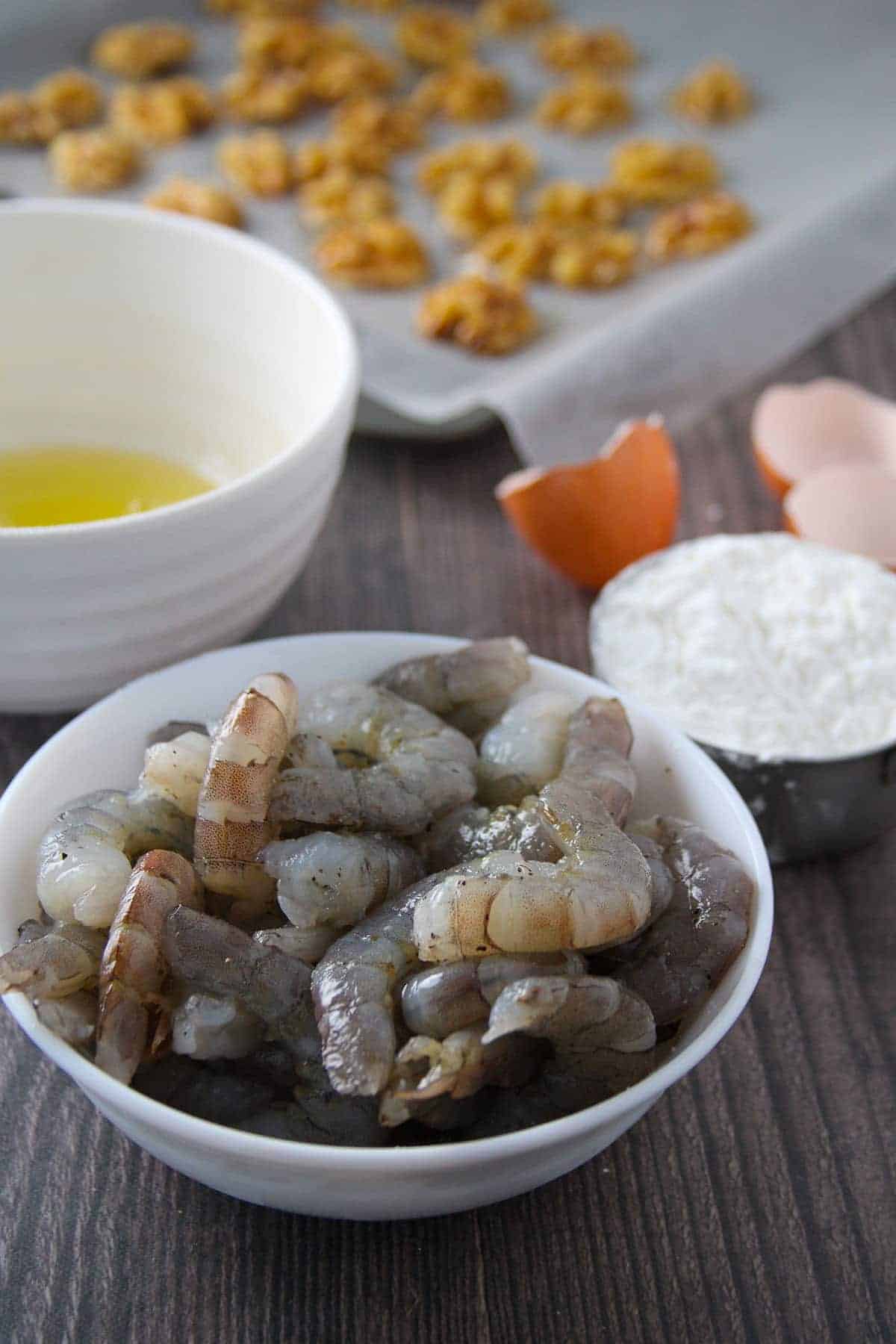 shrimp, egg white, cornstarch in bowls and walnuts on a baking tray