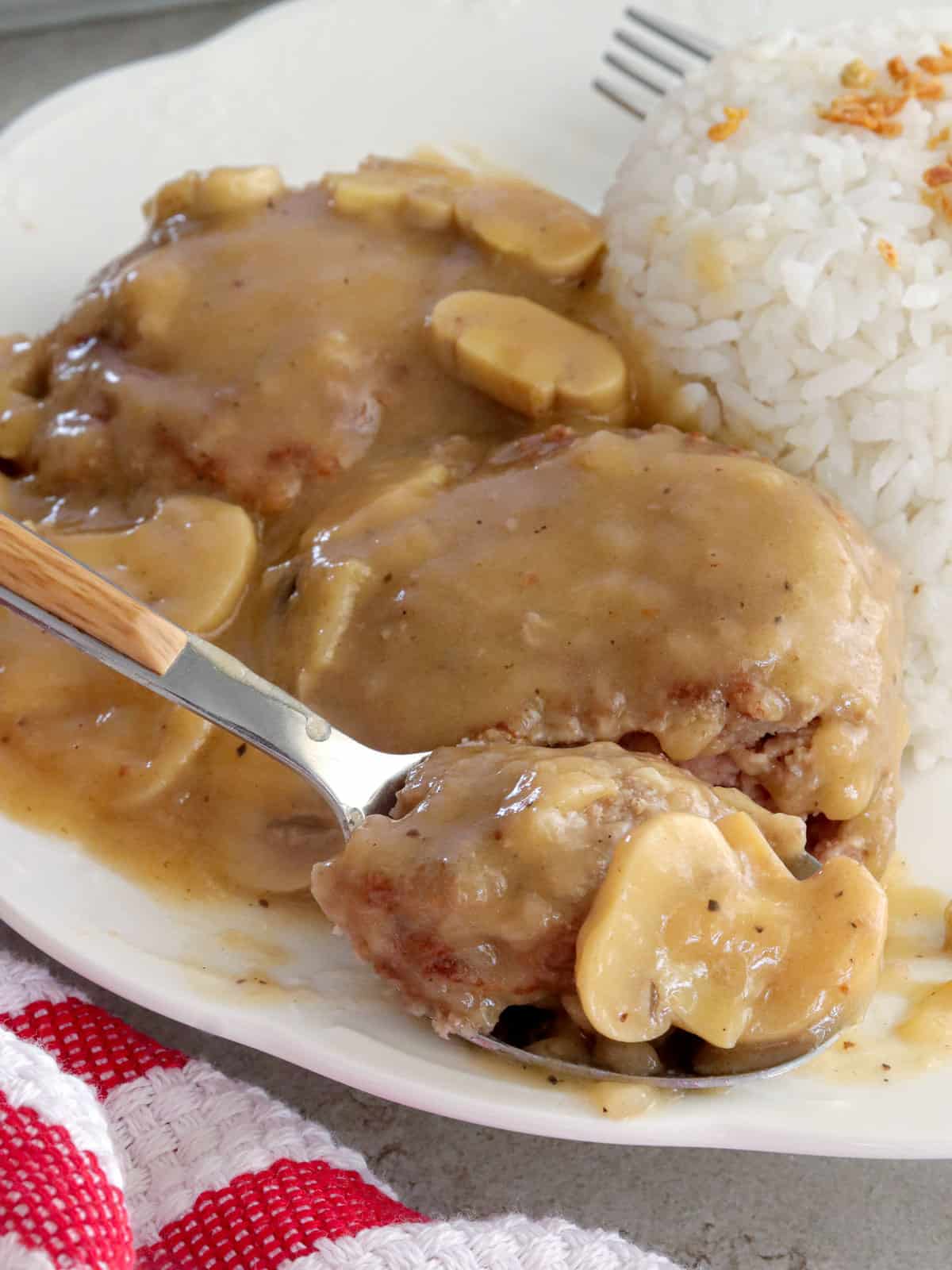 burger steak with mushroom gravy and steamed rice on a white plate.
