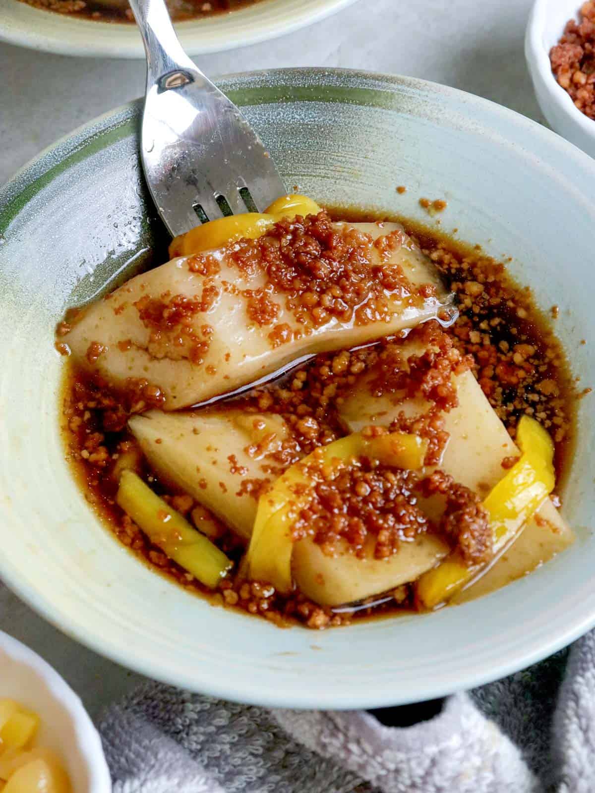 eating kalamay with latik, syrup, and langka with a fork in a bowl