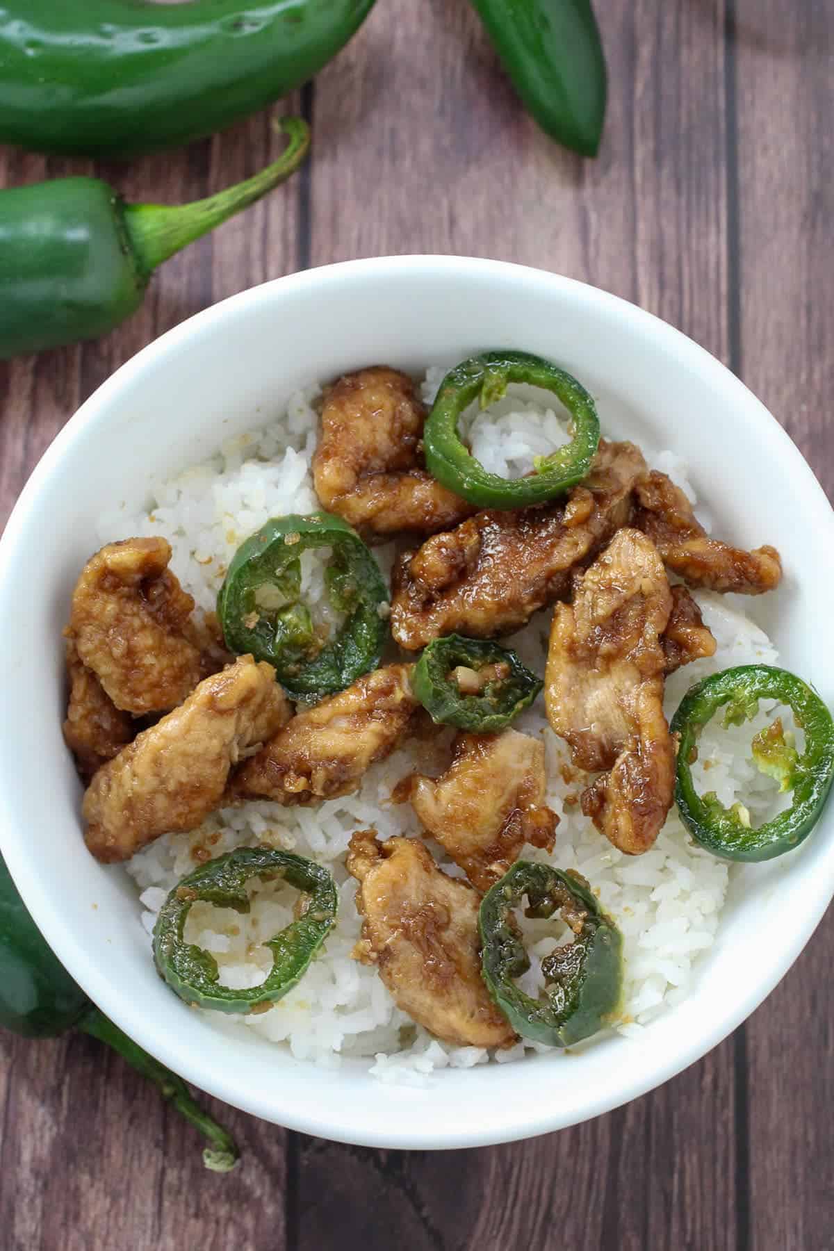 stir-fried chicken with jalapenos over steamed rice in a white bowl
