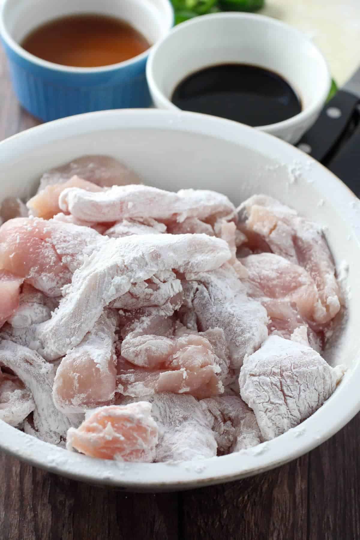 sliced chicken breast coated in cornstarch in a white bowl