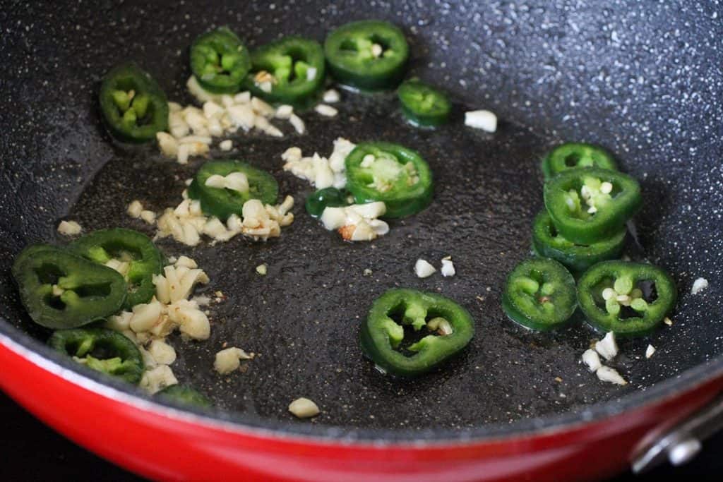 sauteing garlic and jalapeno in a red skillet