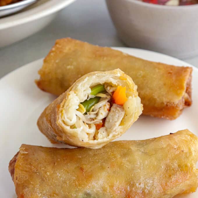 fried lumpia with togue, green beans, carrots, pork and shrimp on a white plate with a bowl of spiced vinegar in the background.