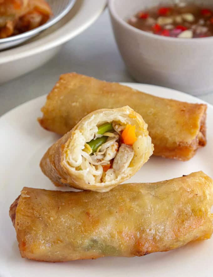 fried lumpia with togue, green beans, carrots, pork and shrimp on a white plate with a bowl of spiced vinegar in the background.
