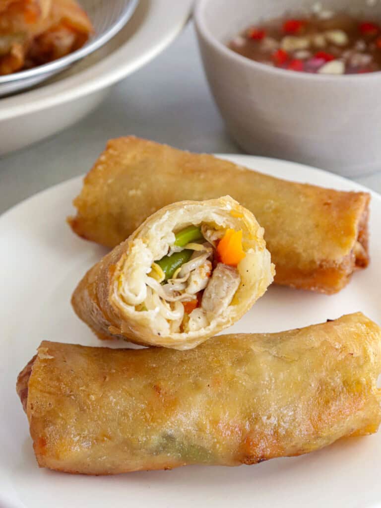 fried lumpia with togue, green beans, carrots, pork and shrimp on a white plate with a bowl of spiced vinegar in the background.