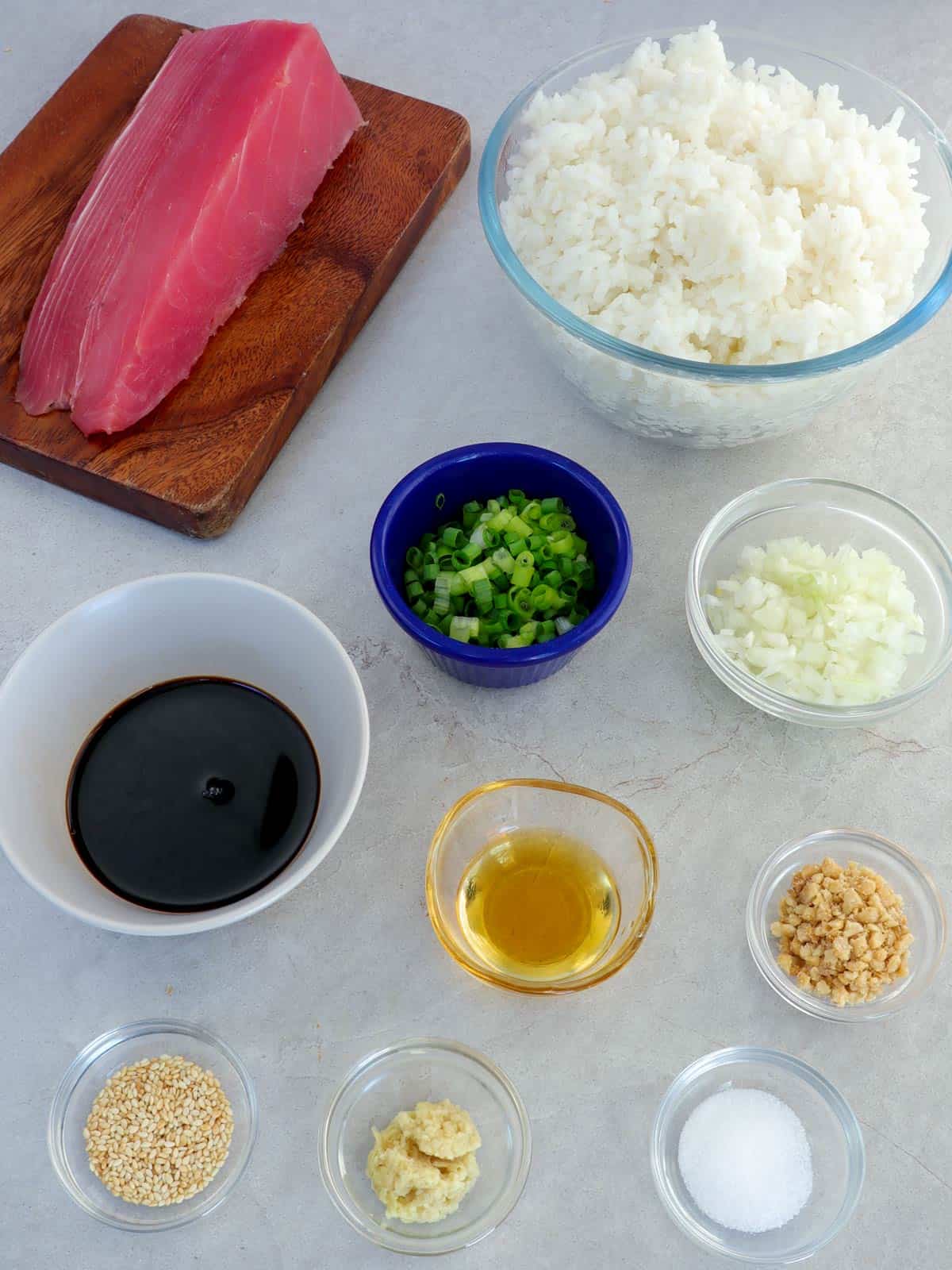 tuna steak, sushi rice, green onions, soy sauce, sesame oil, ground macadamia nuts, sea salt, chopped onions, grated ginger, chopped green onions, and sesame seeds in bowls