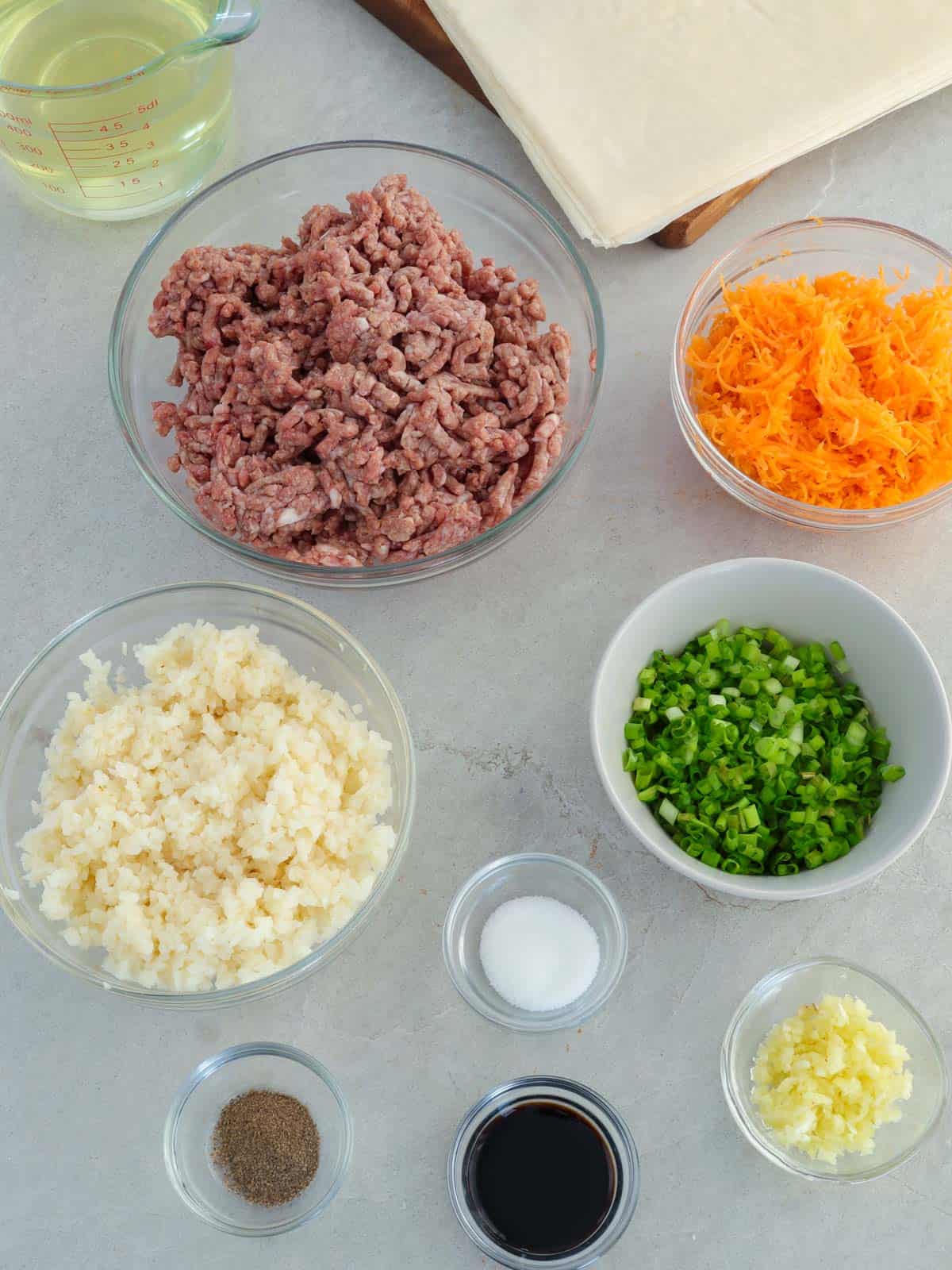 water chestnuts, ground pork, green onions, carrots, garlic, soy sauce, salt, pepper, lumpia wrapper, oil in bowls