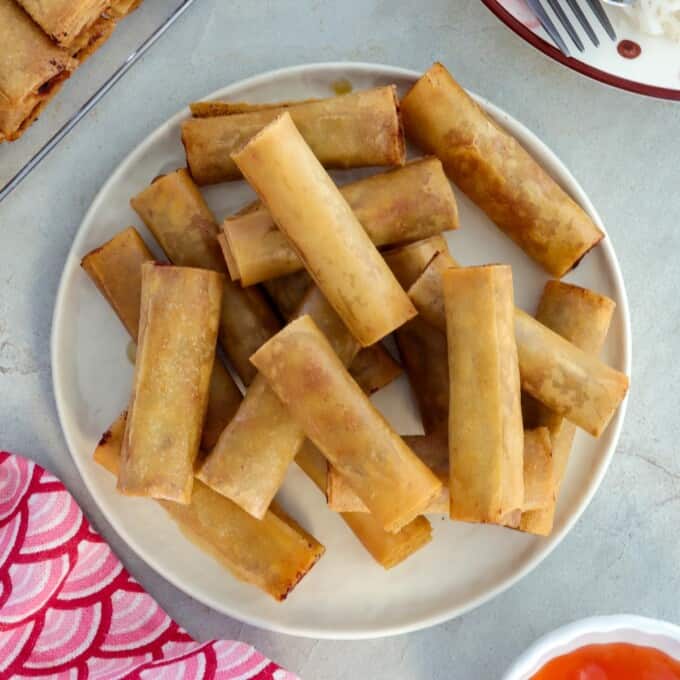filipino springrolls on a white plate with sweet chili sauce on the side