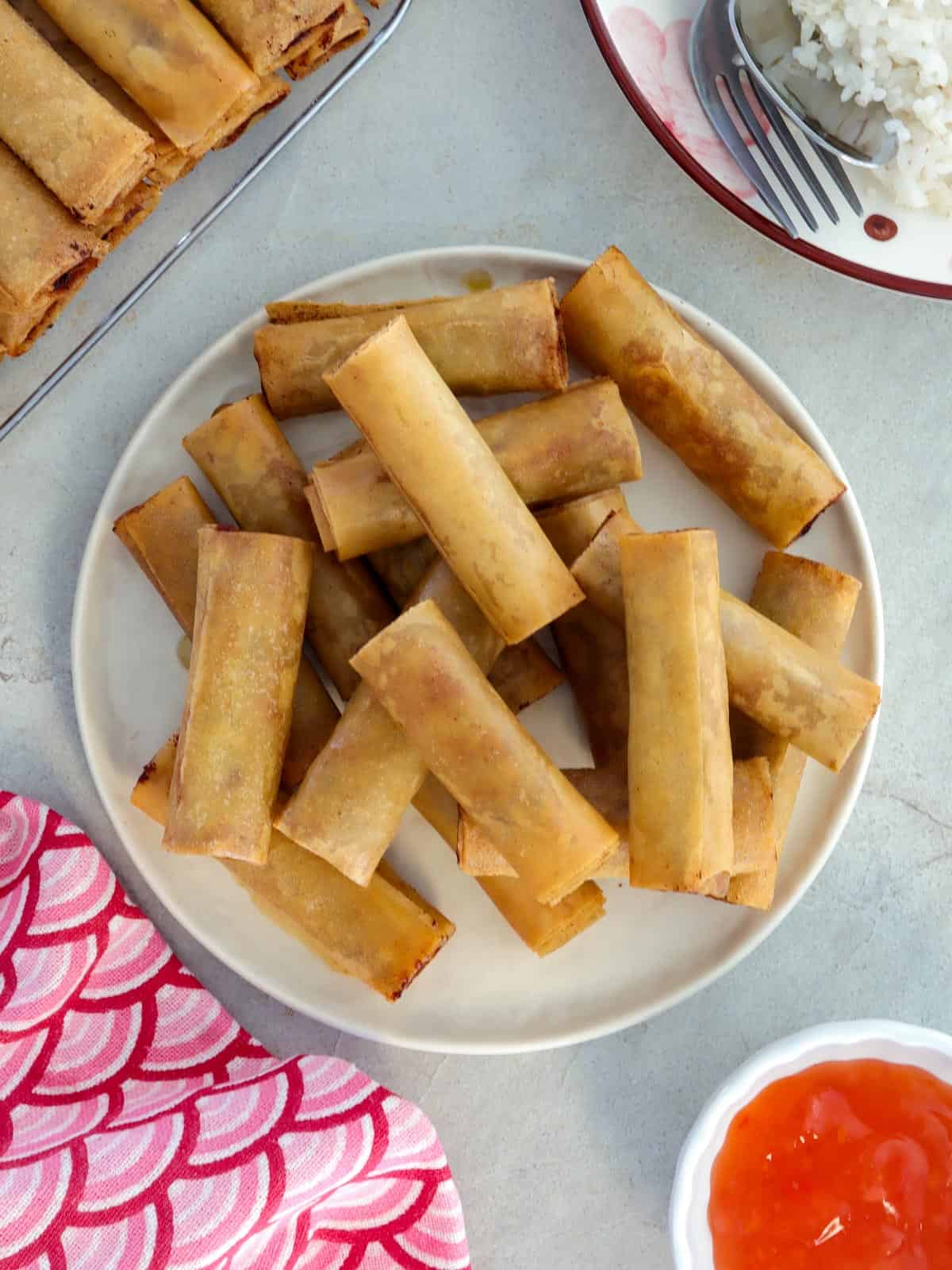 filipino springrolls on a white plate with sweet chili sauce on the side