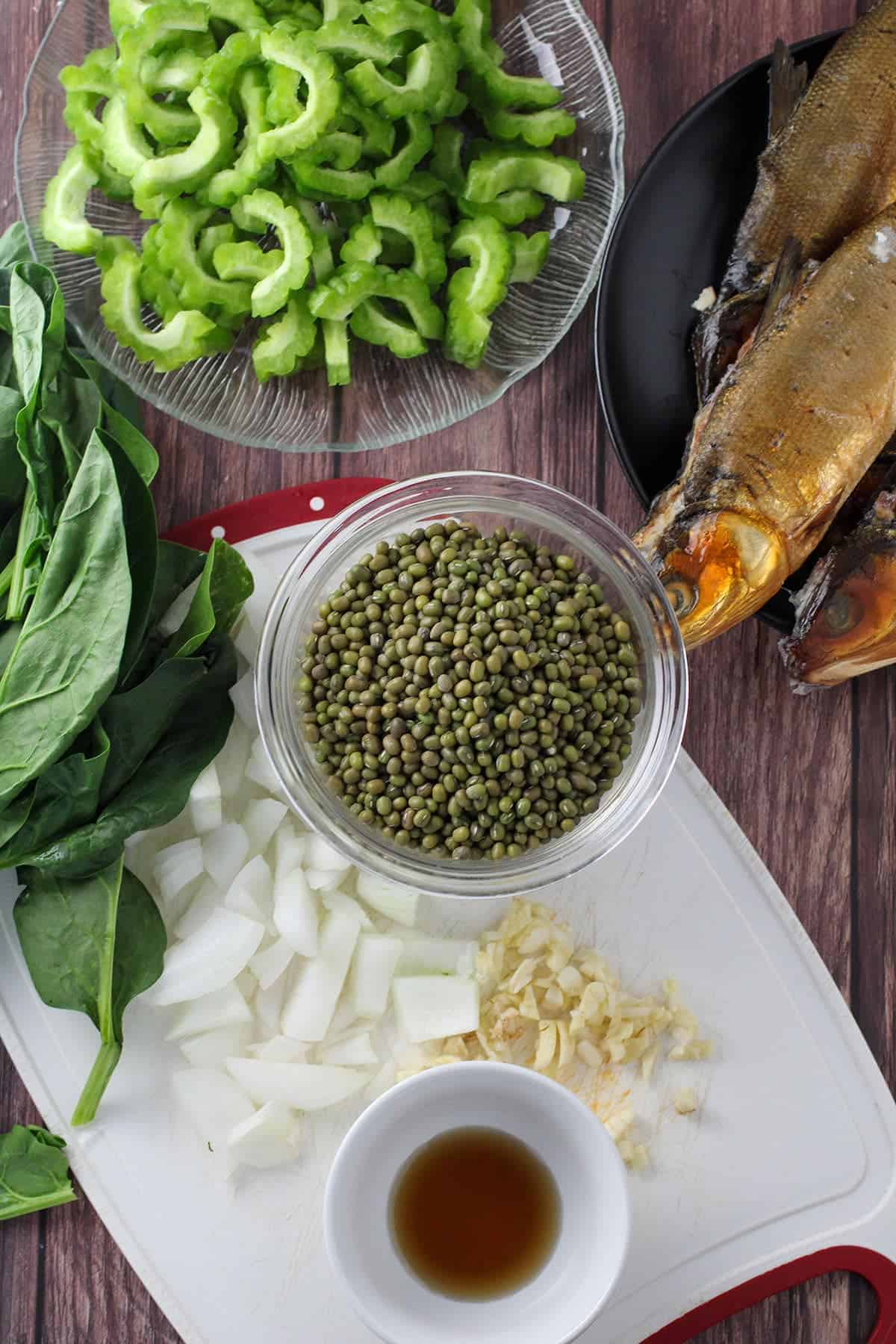 bangus tinapa, sliced ampalaya, mung beans, spinach, chopped onions, and minced garlic on a wood board