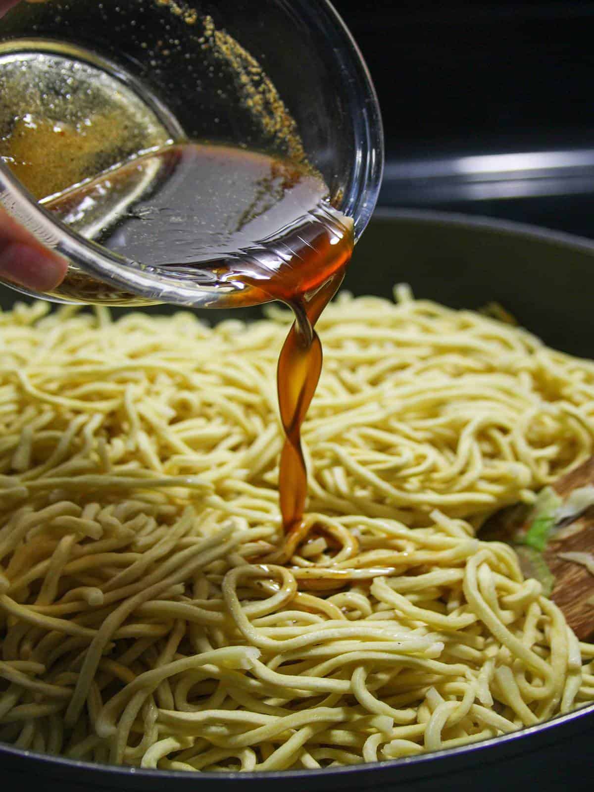 pouring seasoning sauce to a pan of noodles