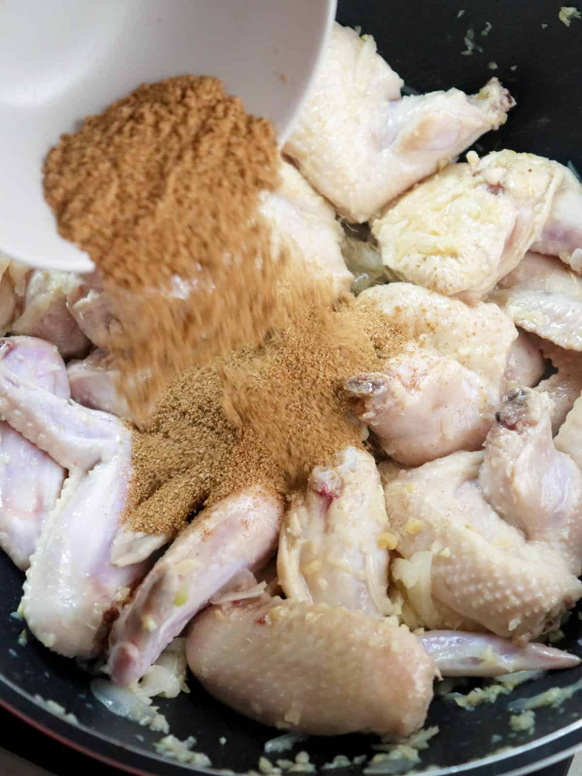 adding tamarind powder to browned chicken in a pan
