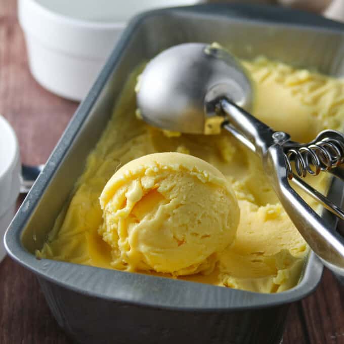 scooping mango ice cream from a metal pan