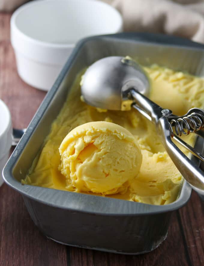 scooping mango ice cream from a metal pan