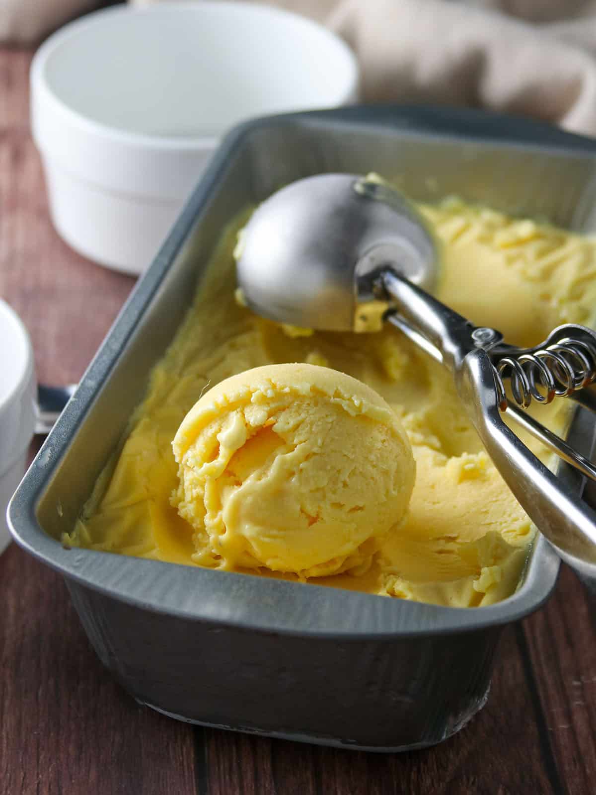 scooping mango ice cream from a metal pan