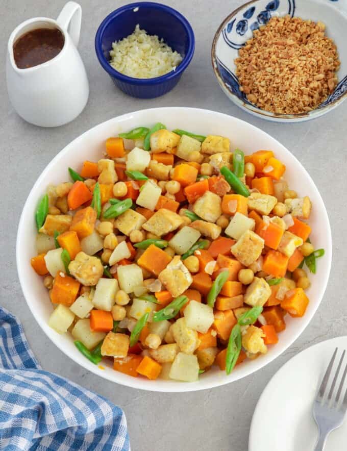 lumpia vegetable filling in a white bowl with bowls of peanut sauce, crushed peanuts, and minced garlic in the background.