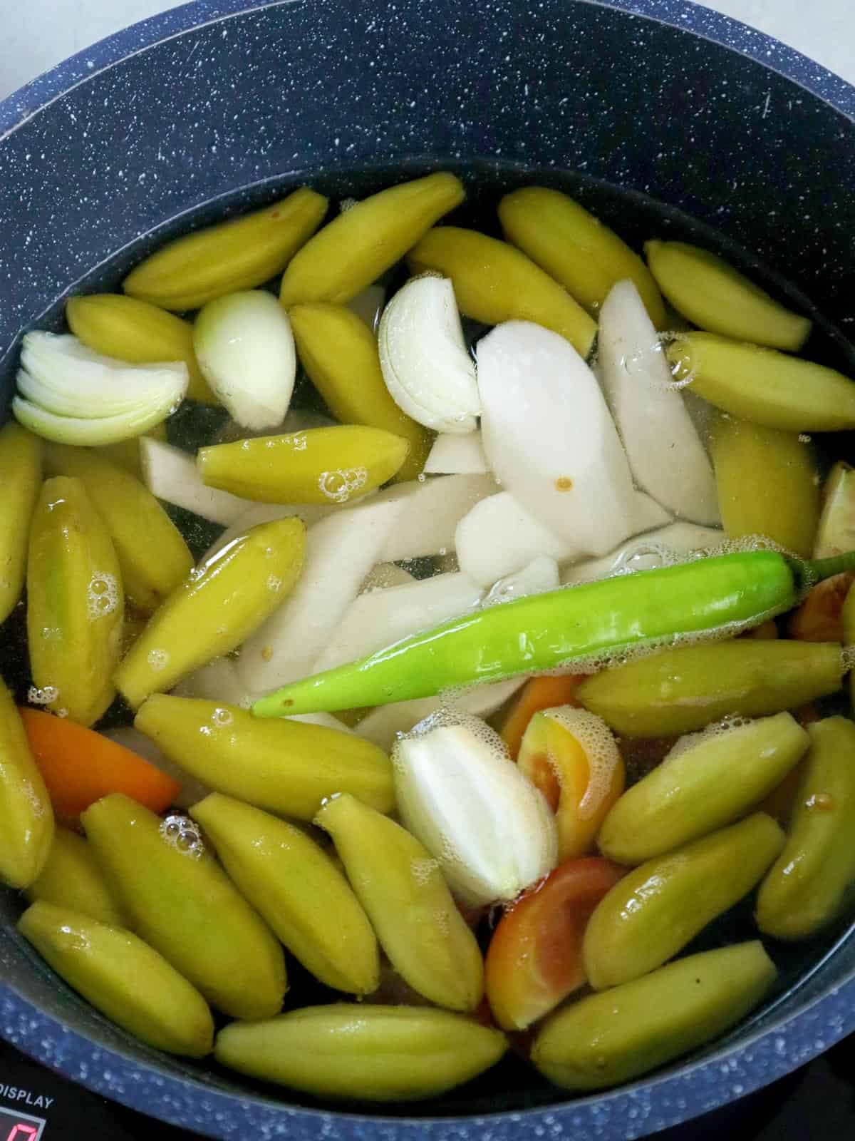 boiling kamias fruit, onions, tomatoes, and chili pepper in a pot of water