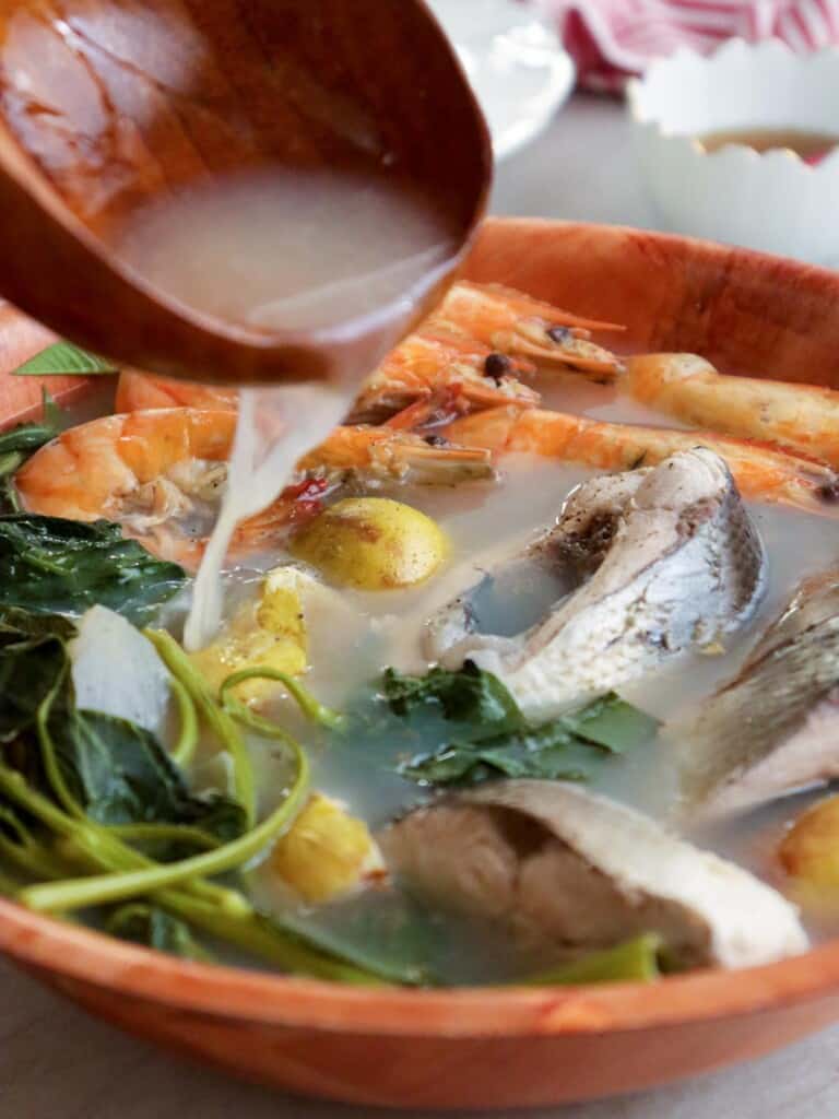 pouring broth on Kapampangan bulanglang with milkfish, shrimp, and guava in a white serving bowl