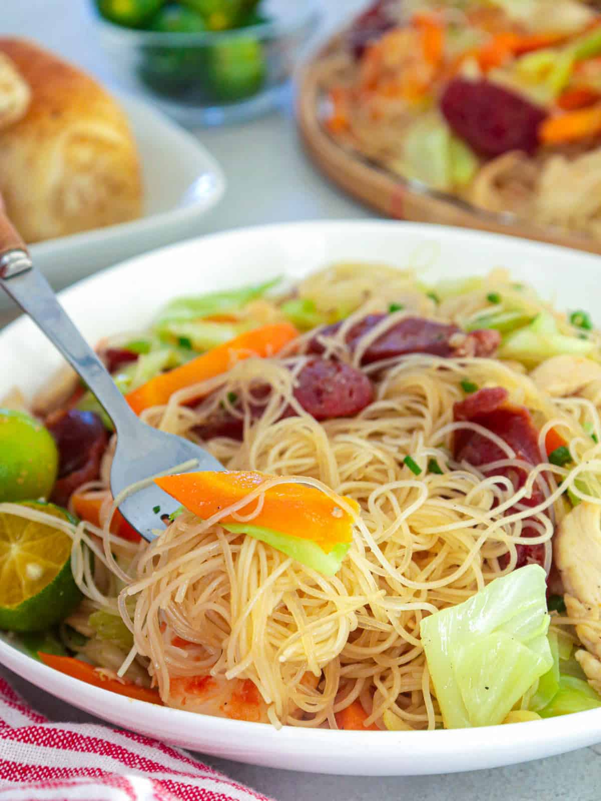 eating pancit bihon in a white bowl with a fork.