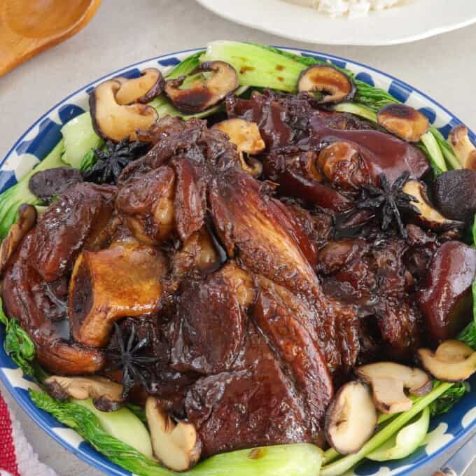 Pata Tim with shiitake mushrooms and bokchoy on a platter with a plate of steamed rice in the background.