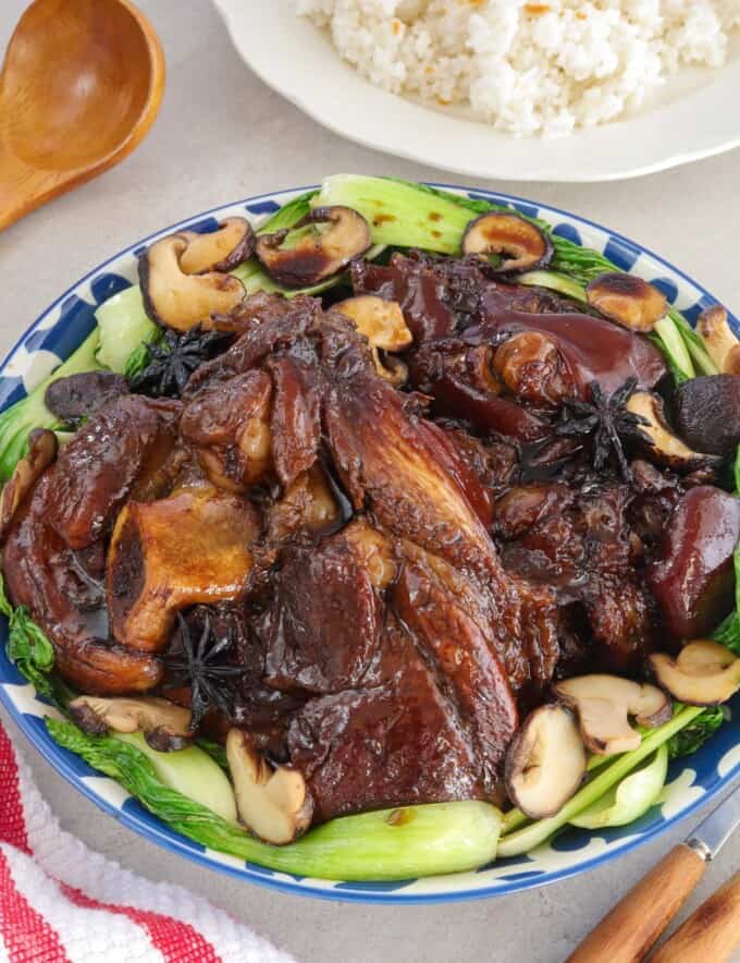 Pata Tim with shiitake mushrooms and bokchoy on a platter with a plate of steamed rice in the background.