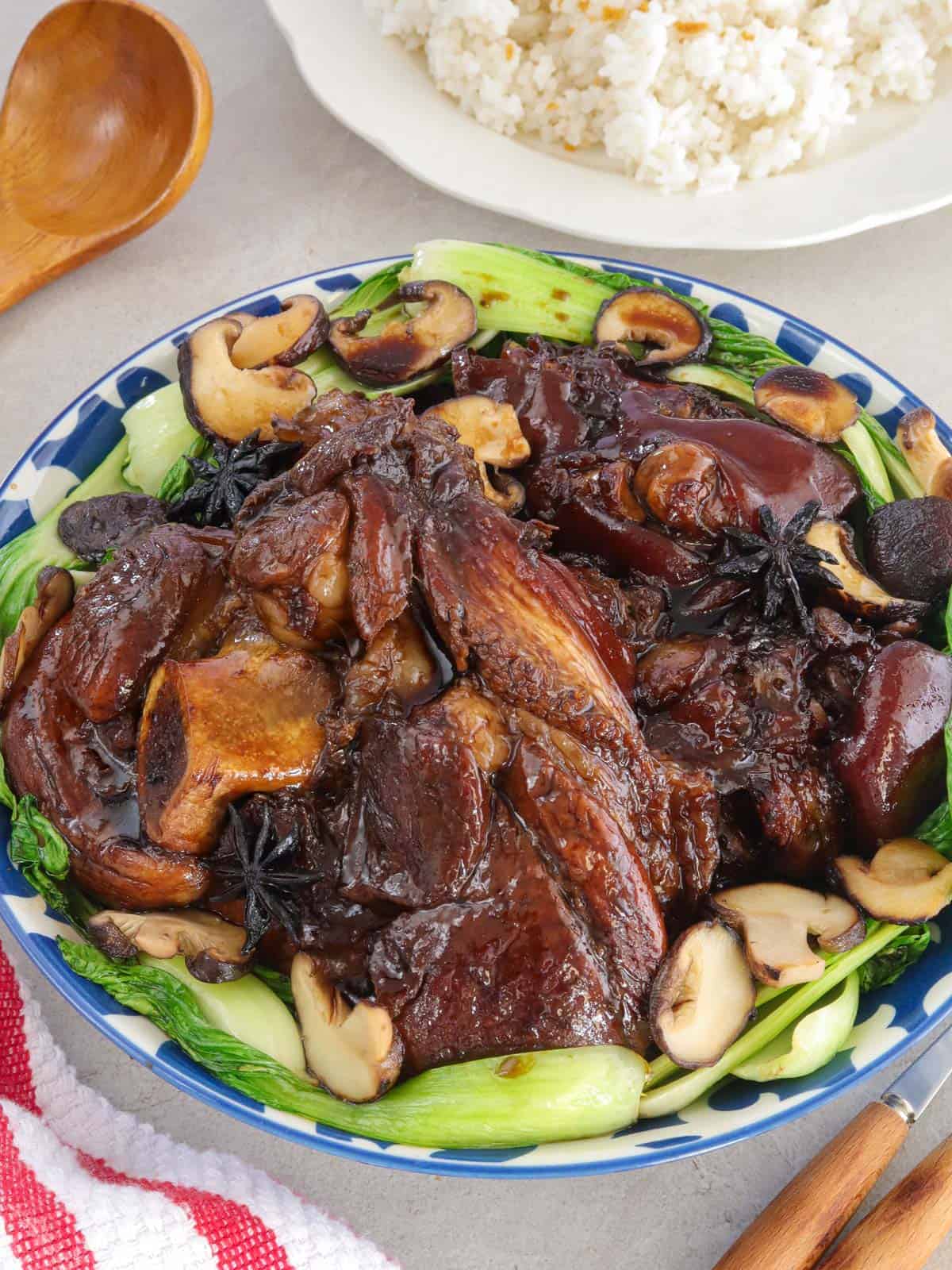 Pata Tim with shiitake mushrooms and bokchoy on a platter with a plate of steamed rice in the background.