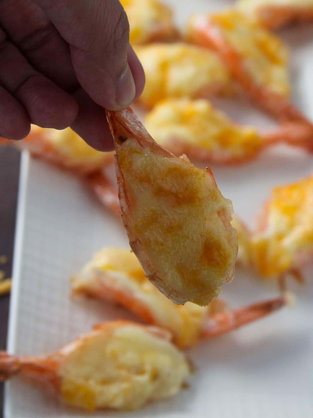 holding cheesy baked shrimp with fingers