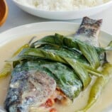 Sinanglay na Tilapia on white serving plate with a plate of steamed rice in the background.