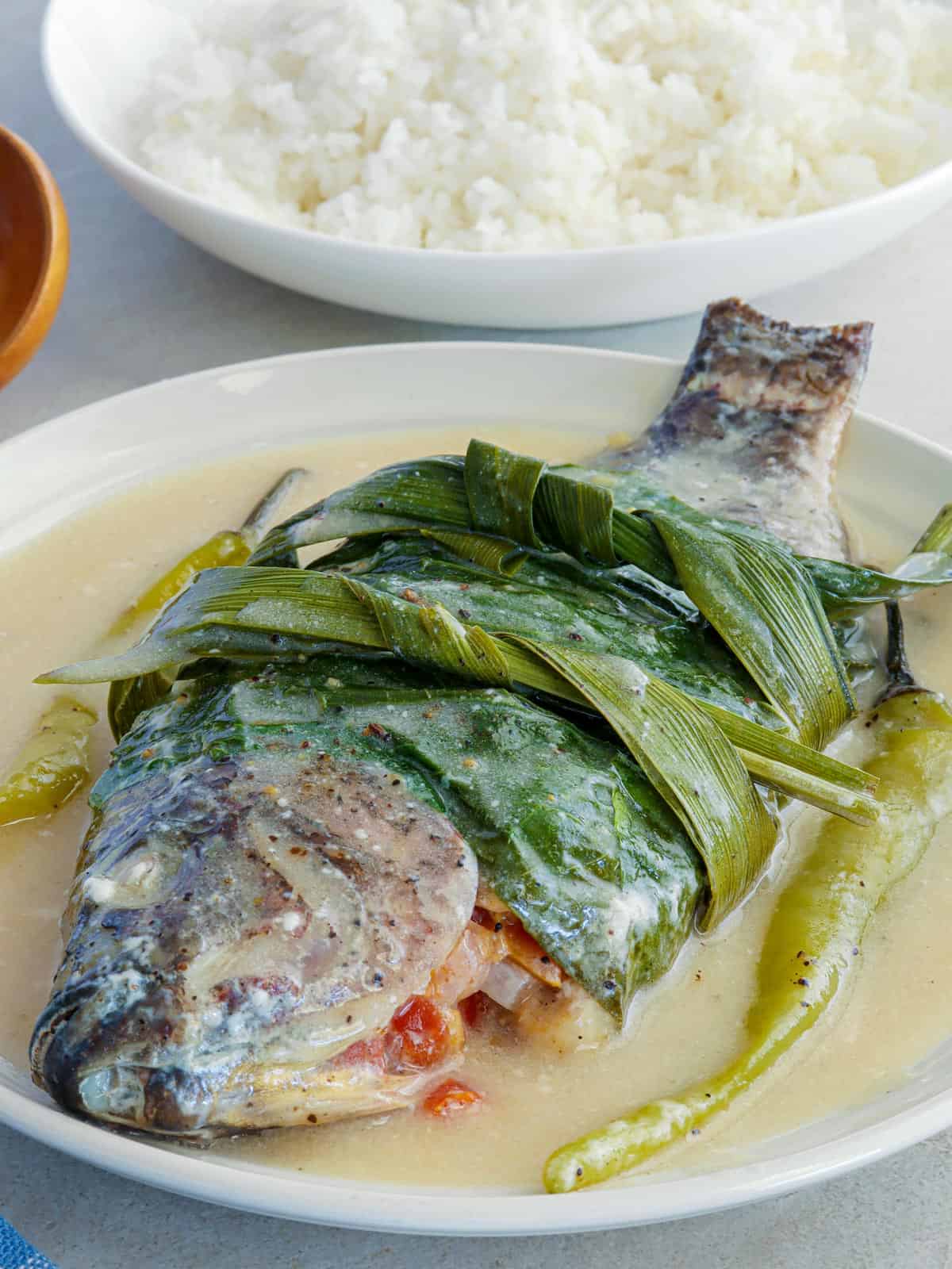 Sinanglay na Tilapia on white serving plate with a plate of steamed rice in the background.