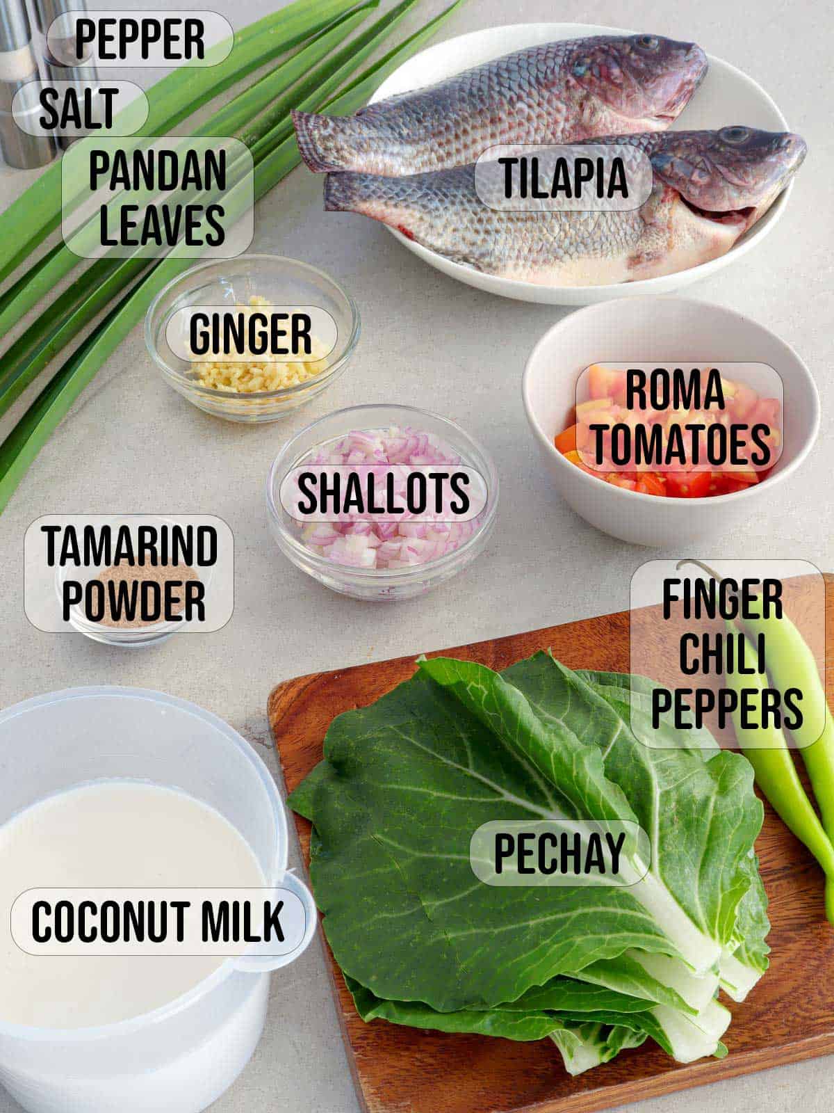 tilapia, pechay leaves, pandan leaf, tomatoes, shallots, tamarind powder, coconut milk, tomatoes, ginger, salt, pepper in bowls.